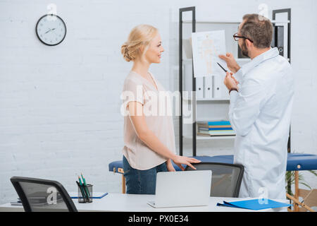 Chiropratica in camice bianco che mostra il corpo umano regime alla paziente di sesso femminile in ospedale Foto Stock