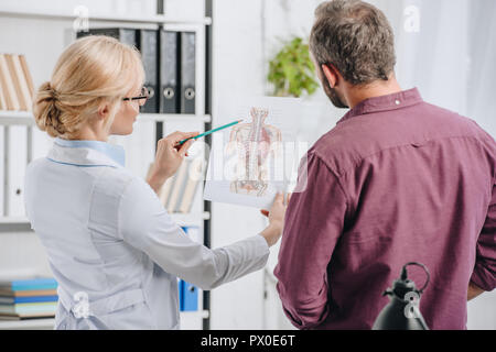 Fisioterapista femmina che mostra il corpo umano foto al paziente in clinica Foto Stock