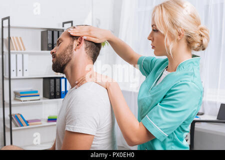 Vista laterale del massaggio femmina terapista facendo massaggio al collo al paziente in clinica Foto Stock