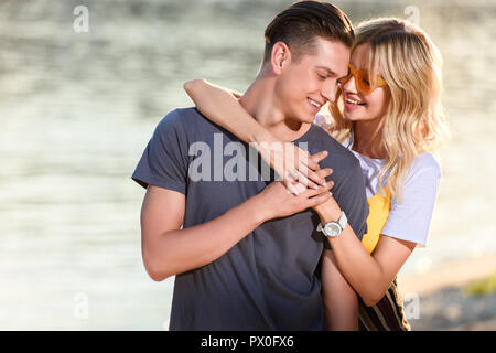 Abbracciando la ragazza ragazzo ed essi toccano con fronte sul fiume spiaggia di sera Foto Stock