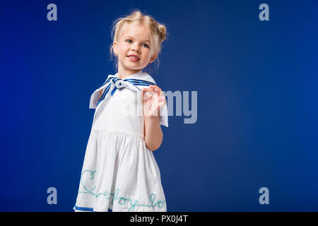 Adorabile bionda kid che pongono in costume da marinaio, isolato su blu Foto Stock