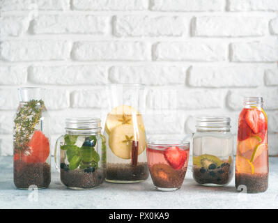 Diversi chia acqua in vetro su uno sfondo grigio. Chia infusa detox acqua con frutti di bosco, frutta ed erbe aromatiche. Mangiare sano, bevande, dieta detox concetto. Copia spazio per il testo Foto Stock