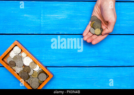 Soldi in mano, scrigno con monete su un blu sullo sfondo di legno, lo spazio per il testo Foto Stock