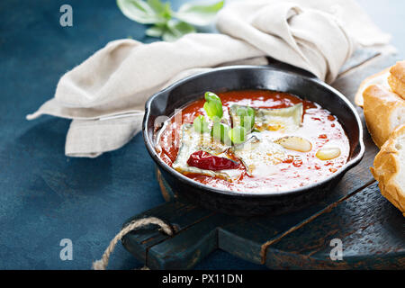 Arrosto di formaggio in salsa di pomodoro con aglio ed erbe in una ghisa pan servita con baguette Foto Stock