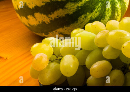 Still Life - un pennello grande di uva verde e anguria in un buio piastra ceramica su uno sfondo di legno Foto Stock