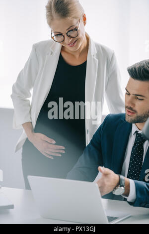 Ritratto di gravidanza imprenditrice e collega al lavoro con il computer portatile a discutere di progetto in ufficio Foto Stock
