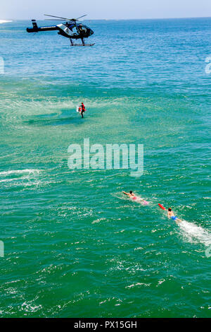 Una città elicottero scende il personale di soccorso di bagnini in acqua per facilitare una vittima di annegamento in un oceano di salvataggio di sicurezza in Huntington Beach, CA. Foto Stock