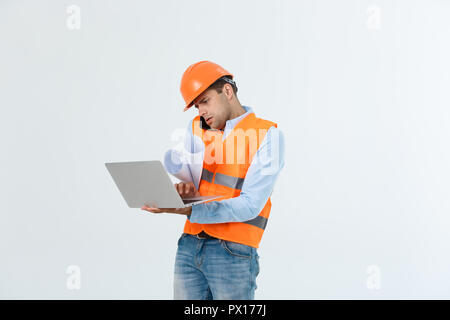 Ingegnere, Architetto, sulla faccia di occupato parla sullo smartphone mentre si trattiene le cianografie. L'uomo, foreman nel casco parlando al telefono, sfondo rosso. Architetto ingegnere chiama per fissare il piano. Concetto di comunicazione Foto Stock