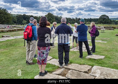 11 Agosto 2018: Northumberland, Regno Unito - visitatori l'ascolto di una guida per un tour al Chesters Roman Fort, il vallo di Adriano, Northumberland, Regno Unito Foto Stock