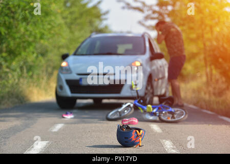 Close-up di un ciclismo casco caduto su asfalto accanto a una bicicletta dopo l incidente di auto sulla strada in città Foto Stock