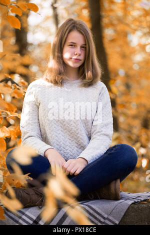 Bella ragazza adolescente seduto nell'autunno del giardino sul recinto , il plaid di lana coperta Foto Stock