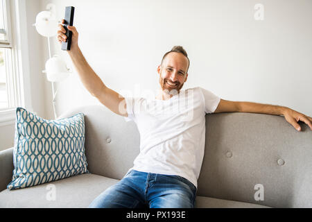 L'uomo a guardare la TV sul divano di casa con il telecomando Foto Stock