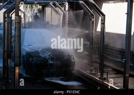 Auto viene lavata a spruzzo in un lavaggio automatico, Auto viene lavata a spruzzo in un lavaggio automatico, lavoratori in background Foto Stock