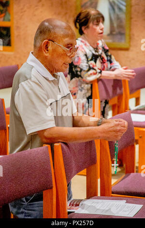 Un anziano vietnamita uomo americano tiene un rosario come egli si inginocchia in preghiera durante la messa in una Laguna Niguel, CA, chiesa cattolica. Foto Stock