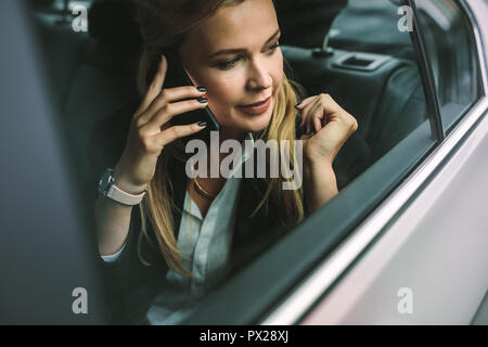 Giovane imprenditrice parlando al cellulare mentre è seduto sul sedile posteriore di un auto. Femmina caucasica executive che viaggiano da un taxi e parlando su mobil Foto Stock