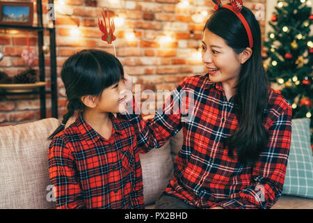 Madre giovane e carina ragazza divertirsi alla vigilia di Natale in salotto. Xmas holiday lifestyle. bellissimo albero di natale e il rosso un muro di mattoni in bac Foto Stock