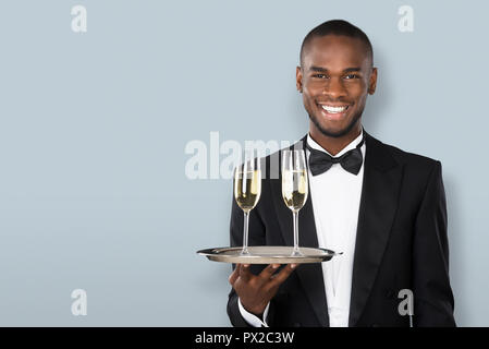 Ritratto di un sorridente cameriere africano Holding Champagne su sfondo grigio Foto Stock