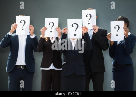 Un gruppo di imprenditori come nascondere le loro facce dietro il punto interrogativo segno su sfondo grigio Foto Stock