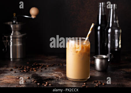 Birra fredda caffè ghiacciato in un bicchiere con latte o creamer su sfondo scuro Foto Stock