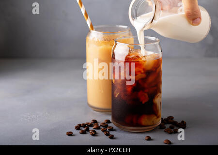 Birra fredda caffè ghiacciato in un bicchiere con latte o creamer versando sopra Foto Stock