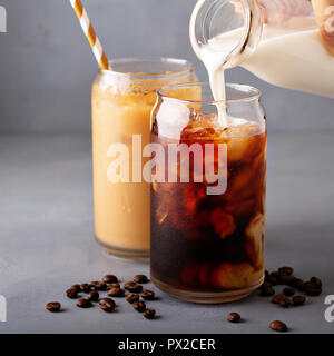 Birra fredda caffè ghiacciato in un bicchiere con latte o creamer versando sopra Foto Stock