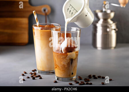 Caffè ghiacciato in bicchieri alti fatto con caffè di cubetti di ghiaccio con latte o creamer versando sopra Foto Stock
