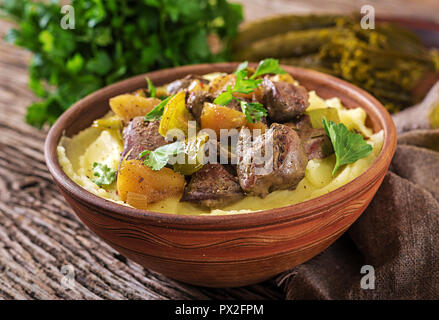 Fritti di fegato di pollo con mele, il peperone e la cipolla con purè di patate come close-up in una ciotola sul tavolo di legno. Foto Stock