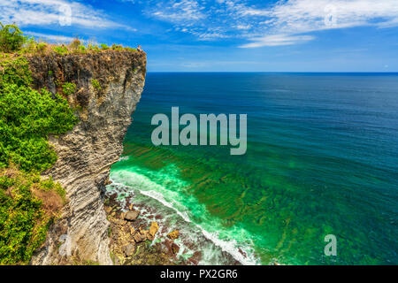 Uomo seduto sul bordo di una scogliera contro lo sfondo di un pittoresco paesaggio tropicale Isola Bali, Indonesia Foto Stock