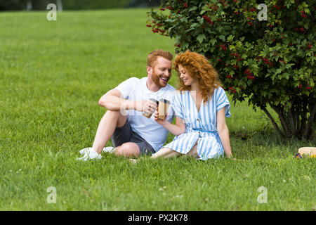 Felice redhead matura il tintinnio di bicchieri di carta con caffè di erba in posizione di parcheggio Foto Stock