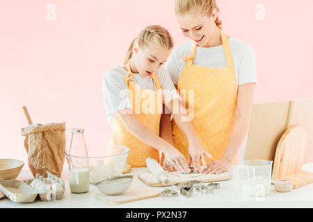 Sorridente madre e figlia di pasta da taglio in forme diverse per i cookie isolato in rosa Foto Stock