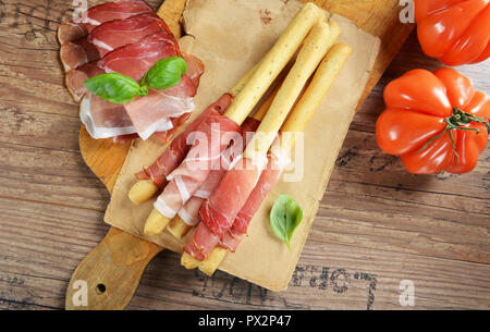 Grissini con prosciutto, olive, basilico sul vecchio sfondo di legno Foto Stock