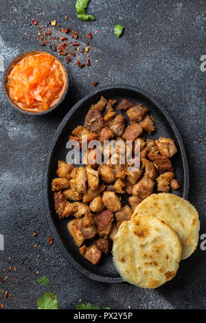 Cibo colombiano. Maiale fritto CHICHARRON, AREPAS colombiano e salsa di pomodoro. Vista dall'alto. Sfondo nero Foto Stock