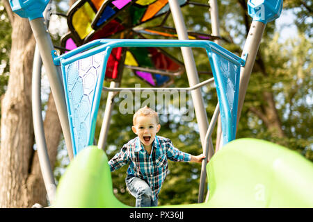 Little Boy divertirsi su un parco giochi all'aperto in estate. Bambino su una diapositiva. Foto Stock