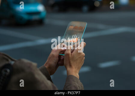 Chiudere in su su una mano femminile che è in possesso di un telefono cellulare trasparente gadget concetto, utilizzando un'app con un grafico i dati di un grafico Foto Stock