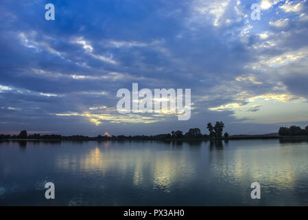 Serata di scure nuvole durante il tramonto su un lago calmo Foto Stock