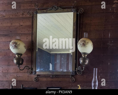 Interno del vintage Home texano con parete a specchio sulla parete in legno & 2 parete lampade decorative. Orizzontale. Piazza di castagno villaggio storico, McKinney,Texas Foto Stock