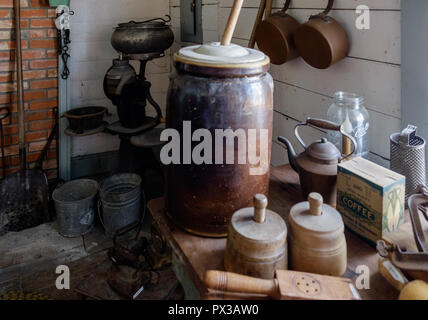 Interno del vintage Home texano con burro di antiquariato i bidoni e gli altri articoli per la cucina. Muro di mattoni, pala. Piazza di castagno villaggio storico, McKinney,Texa Foto Stock