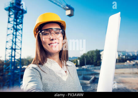 Bella donna ingegnere civile sta prendendo un autoritratto nel suo lavoro di fronte ad una gru Foto Stock