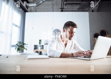 Un giovane uomo che lavora sul suo computer portatile sotto l'orologio. Comunicare su business, tecnologia, scadenze, focus, concetration, produttività Foto Stock