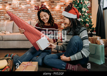 Asian le giovani ragazze divertirsi doni di incarto a casa. Un grande lavoro di squadra di imballaggio amici regali per Natale. prepararsi per i prossimi anno nuovo e xmas Foto Stock