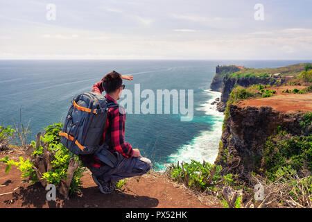 Fotografo di viaggio con zaino foto LovePro WHISTLER 350 godono di vista la natura vista del paesaggio di Uluwatu scogliera con padiglione e il blu del mare di Bali Foto Stock