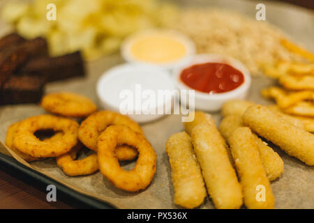 La birra lager e spuntini su un tavolo di legno. Dadi, chips, arachidi, toast, cracker. Antipasto fast food. La birra artigianale. Beerboard. Formaggio di pomodoro e aglio sauc Foto Stock