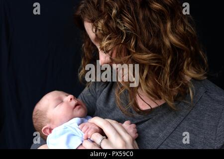 Madre teneramente guardando il neonato contro uno sfondo nero Foto Stock