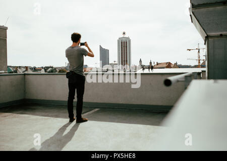 Foto di vista posteriore del giovane di fotografare una skyline della città con il suo smartphone Foto Stock