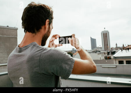 Close-up foto di vista posteriore del giovane di fotografare una skyline della città con il suo smartphone Foto Stock