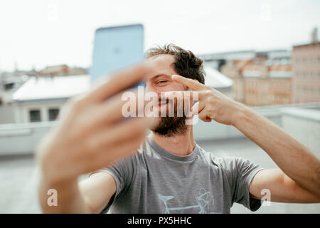 Vista frontale del giovane uomo barbuto fotografare se stesso con il suo smartphone Foto Stock
