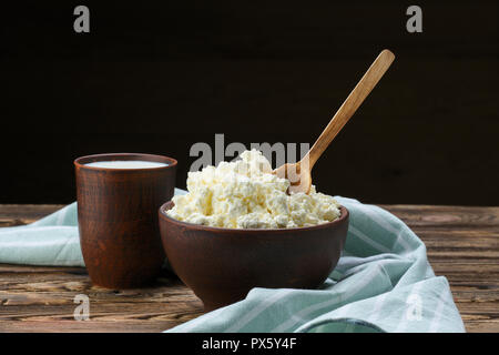 Per la ricotta con il cucchiaio di legno in esso e il latte in clayware sul tavolo di legno Foto Stock