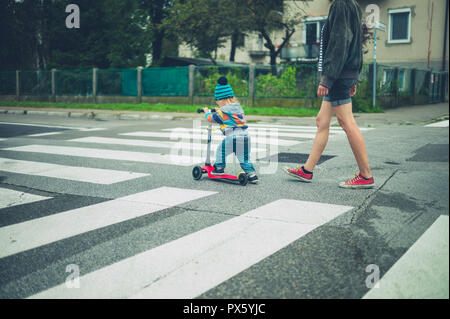 Una madre e un bambino su uno scooter sono a piedi sul crosswalks Foto Stock