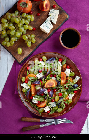 Sana insalata di autunno con cioccolato persimmon, Formaggi a Muffa Blu, Verde uva, prugna e rucola su una piastra di argilla con aceto di vino dolce medicazione, verticale Foto Stock