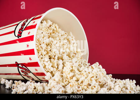 Eventuali fuoriuscite di popcorn casella sulla scrivania nero e sfondo rosso. Retro bianco e rosso. Cinema e Film concetto alimentare. Close up, il fuoco selettivo Foto Stock